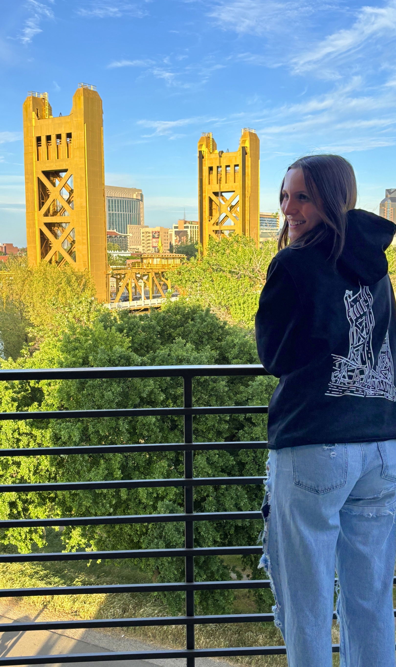Maret, founder of pax, wearing a pax sweatshirt with Sacramento's Tower Bridge in the background